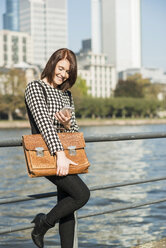 Deutschland, Frankfurt, junge Geschäftsfrau am Flussufer mit Mobiltelefon - UUF002487