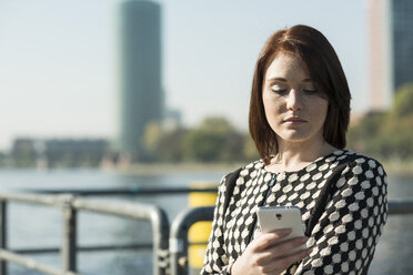 Germany, Frankfurt, young businesswoman by the riverside with cell phone - UUF002490