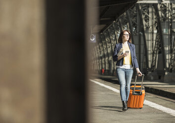 Junge Frau mit Mobiltelefon und Gepäck am Bahnhof - UUF002504