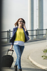 Lächelnde junge Frau mit Gepäck auf einem Mobiltelefon - UUF002511