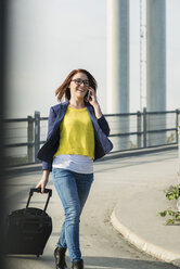 Smiling young woman with baggage on cell phone - UUF002511