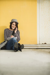 Junge Frau auf dem Boden sitzend mit Notebook und Mobiltelefon - UUF002526