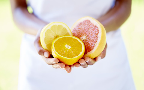 Frauenhände halten Orangen- und Grapefruithälften, lizenzfreies Stockfoto