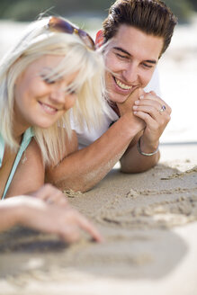 Junges Paar liegt am Strand und zeichnet in den Sand - ZEF002364