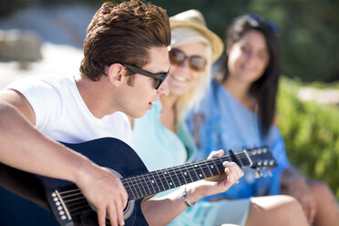 Freunde schauen auf einen jungen Mann, der Akustikgitarre spielt - ZEF002370