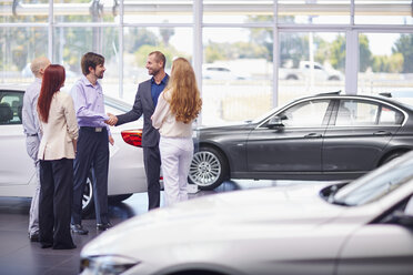 Car dealer meeting with clients in showroom - ZEF002039