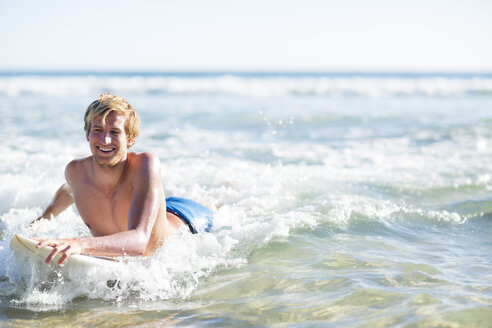 Glücklicher junger Mann auf einem Surfbrett im Meer liegend - ZEF002401