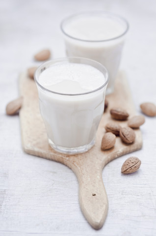 Zwei Gläser mit hausgemachter Mandelmilch und Mandeln auf einem Holzbrett, lizenzfreies Stockfoto