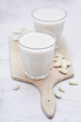 Zwei Gläser mit hausgemachter Mandelmilch und geschälten Mandeln auf einem Holzbrett, lizenzfreies Stockfoto