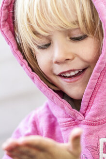 Porträt eines lächelnden kleinen Mädchens, das etwas auf der Hand beobachtet - JFEF000517