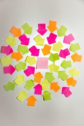 Coloured arrow shaped adhesive notes and a square one on white wall - SARF000988