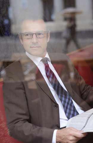 Geschäftsmann sitzt in einem Café mit Zeitung und beobachtet etwas, lizenzfreies Stockfoto