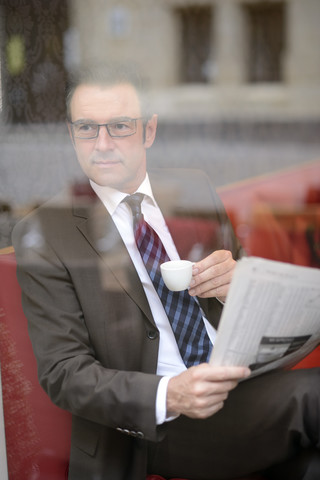 Geschäftsmann sitzt in einem Café mit Zeitung und beobachtet etwas, lizenzfreies Stockfoto