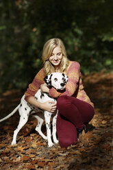 Lächelnde blonde Frau mit Dalmatiner im herbstlichen Wald - GDF000543