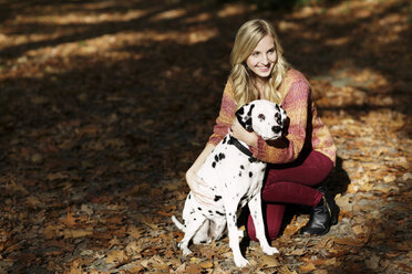 Lächelnde blonde Frau mit Dalmatiner im herbstlichen Wald - GDF000544