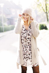 Porträt einer lächelnden blonden Frau in gemustertem Kleid, Strickjacke und Wollmütze - GDF000545