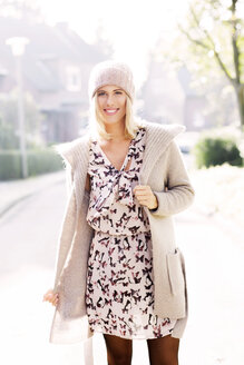 Portrait of smiling blond woman wearing patterned dress, cardigan and wool cap - GDF000546