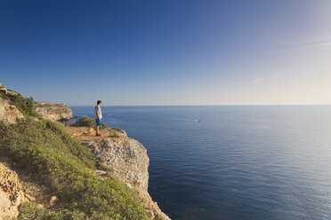 Spanien, Balearen, Mallorca, ein Jugendlicher steht auf einem Felsen an der Steilküste und beobachtet den Sonnenuntergang - MSF004357