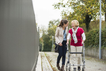 Erwachsene Enkelin, die ihrer Großmutter beim Gehen mit einer Gehhilfe auf Rädern hilft - UUF002534