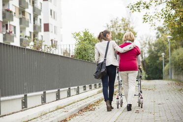 Adult granddaughter assisting her grandmother walking with wheeled walker, back view - UUF002535