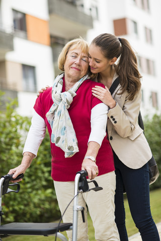 Enkelin, die ihrer Großmutter beim Gehen mit dem Rollator hilft, lizenzfreies Stockfoto