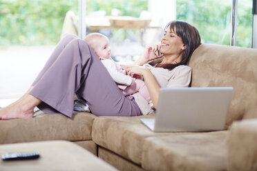 Mutter sitzt mit Baby auf der Couch und spricht mit dem Handy - ZEF002284