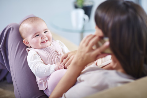 Mutter mit Baby auf der Couch im Gespräch mit dem Handy, lizenzfreies Stockfoto