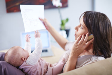 Mutter mit Baby auf der Couch, die mit ihrem Handy telefoniert und sich Papiere anschaut - ZEF002286