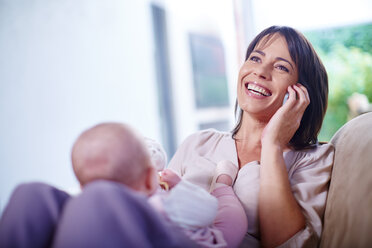 Mother with baby on couch talking on cell phone - ZEF002288