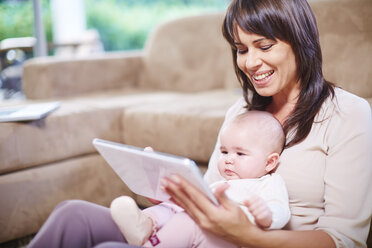 Mother with baby in living room using digital tablet - ZEF002290
