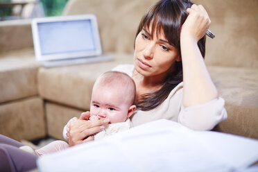 Mutter hält ihr Baby, während sie von zu Hause aus arbeitet - ZEF002294