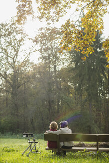 Senior woman and granddaughter sitting on a park bench, back view - UUF002625