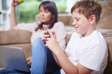 Junge sitzt neben seiner Mutter und schreibt eine SMS auf seinem Handy - ZEF002298
