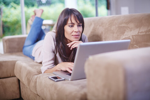 Frau liegt auf der Couch und benutzt einen Laptop - ZEF002303