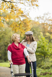 Ältere Frau und ihre fürsorgliche erwachsene Enkelin gehen gemeinsam in einem herbstlichen Park spazieren - UUF002585