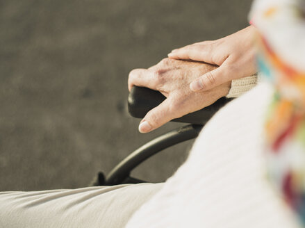 Young woman's hand on hand of senior woman sitting in wheelchair - UUF002593