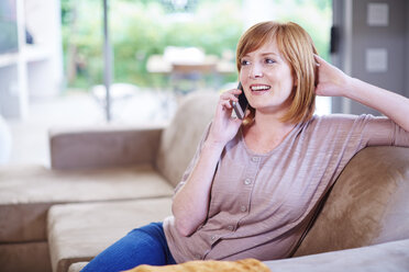 Woman sitting on couch and talking on cell phone - ZEF002276