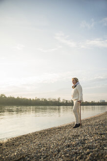Ältere Frau mit Spazierstock steht am Ufer und beobachtet den Sonnenuntergang - UUF002614