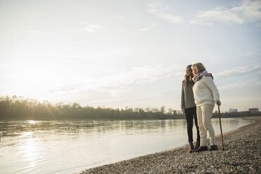 Young woman and her grandmother standing together at water watching sunset - UUF002616