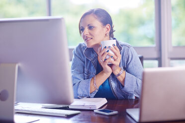 Smiling woman at desk holding a coffee cup - ZEF002323