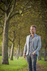 Smiling young businessman standing in a park - PAF001072