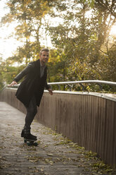 Lächelnder junger Mann beim Skateboardfahren auf einer Fußgängerbrücke im Herbst - PAF001089