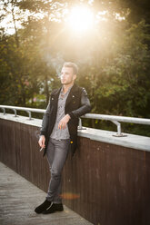 Young man smoking a cigarette on a footbridge at backlight - PAF001081