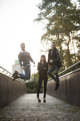 Two young men jumping into the air on a footbridge while young woman watching - PAF001090