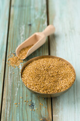 Bowl of golden linseed and shovel on green wood - MYF000693