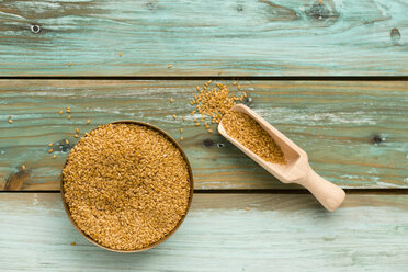 Bowl of golden linseed and shovel on green wood - MYF000694