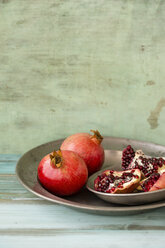 Metal dishes of whole and sliced pomegranates on wood - MYF000696