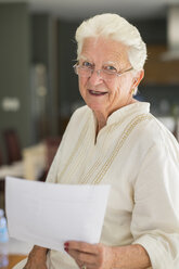 Porträt einer lächelnden älteren Frau mit Brille, die ein Blatt Papier hält - ABAF001574