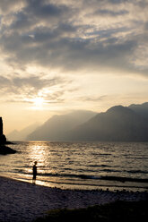 Italy, Veneto, Malcesine, Boy standing at Lake Garda in evening light - LVF002169