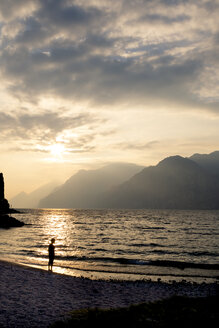 Italien, Venetien, Malcesine, Junge steht am Gardasee im Abendlicht - LVF002169